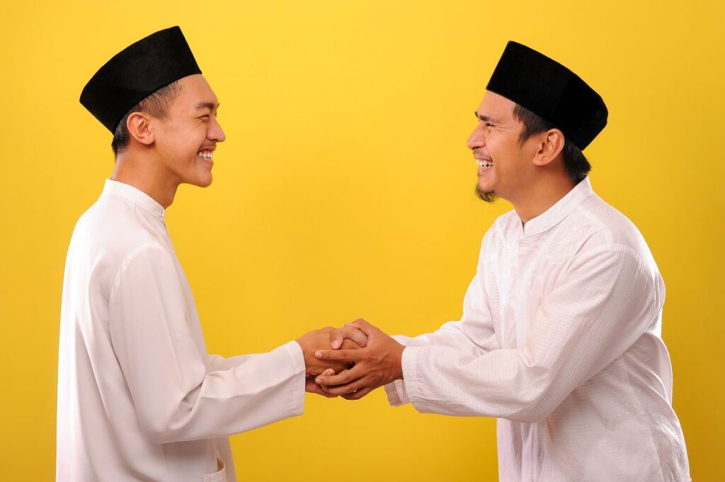 dua orang sedang berjabat tangan dengan latar kuning, berbaju koko, menggunakan Peci