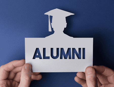 Tangan memegang kertas dengan tampilan orang memakai topi kelulusan dengan tulisan Alumni